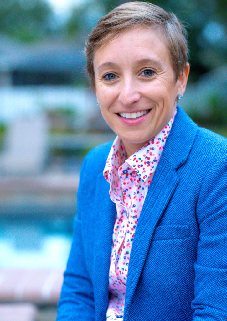 Skeeter Little, Realtor with Kemp Realty Group, smiling in a blue blazer, seated outdoors near a pool.